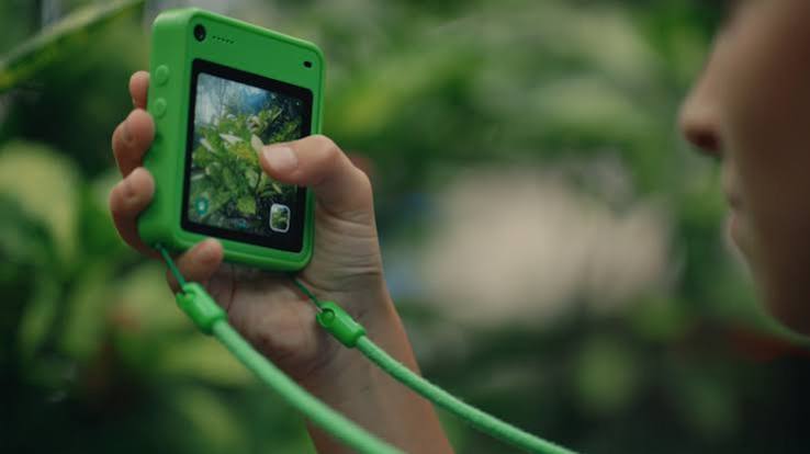 A child holding a bright green Freckle phone on a lanyard, its screen showing green leaves