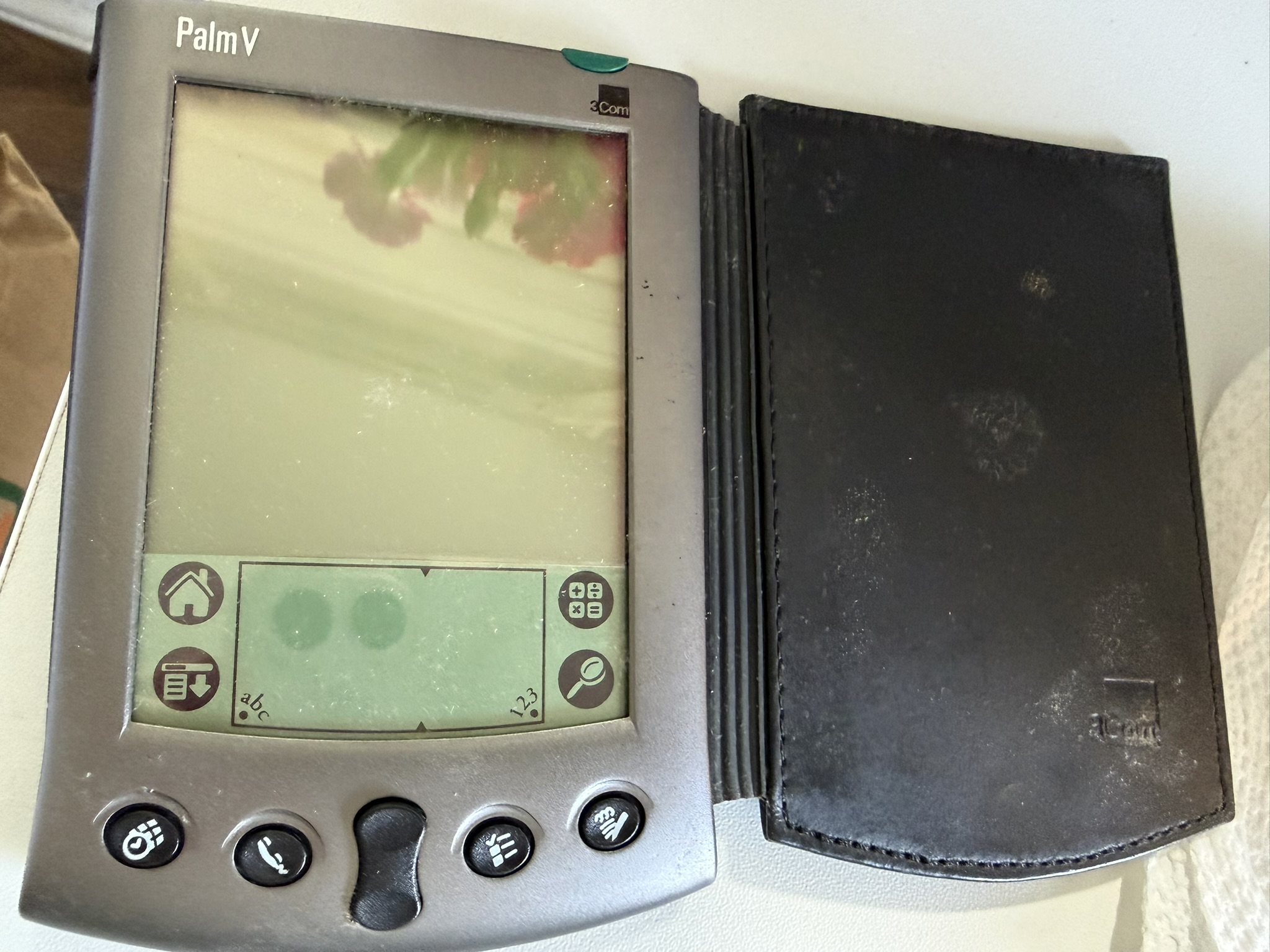 A silver 3Com Palm V PDA open in its worn black leather case